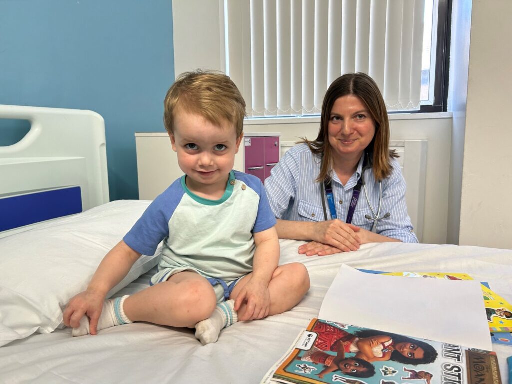 An image with a Eddie a young patient on the bed with Dr Aida Semic-Jusufagic, sitting at the bed side.