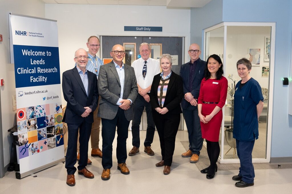 An image of key clinical staff and colleagues standing smiling in a line up photo with Karin Smyth MP stood in the centre outside the NIHR Leeds Clinical Research Facility St James site.